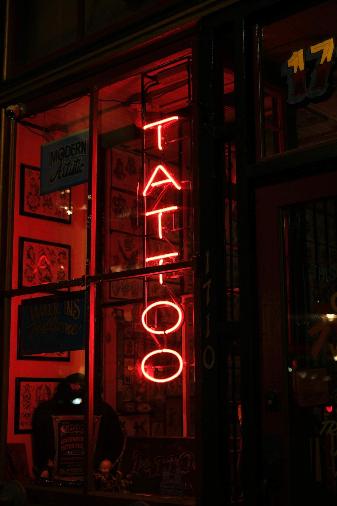 A red neon sign advertises a tattoo parlor.