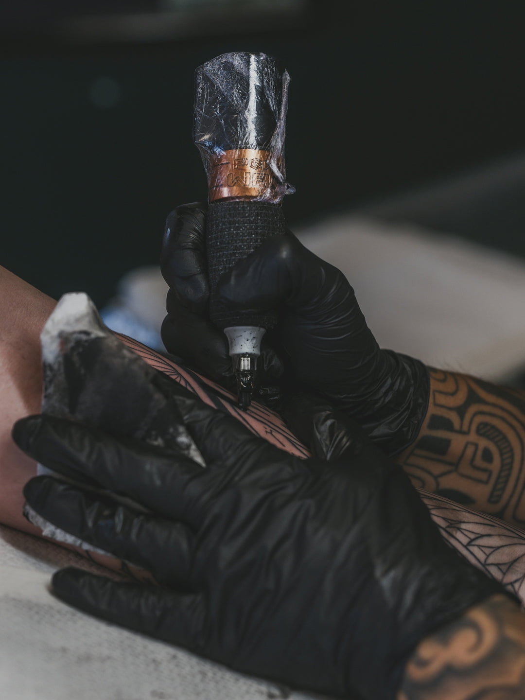 Artist tattooing a design onto a person's arm.