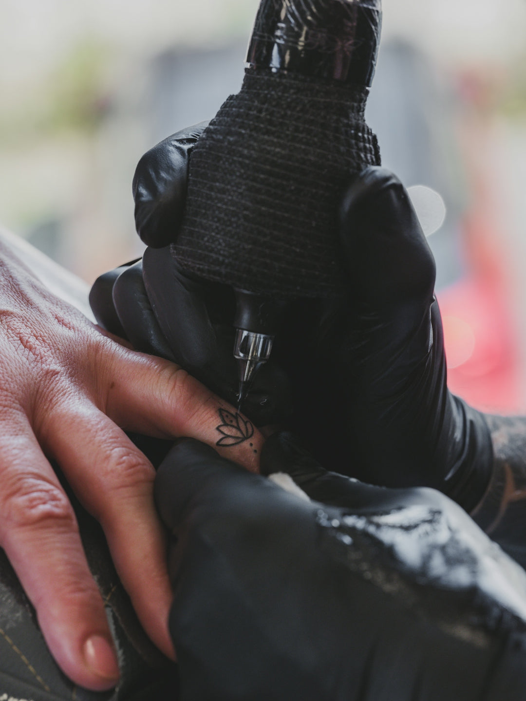 Tattoo artist with black gloves inks finger with a machine.