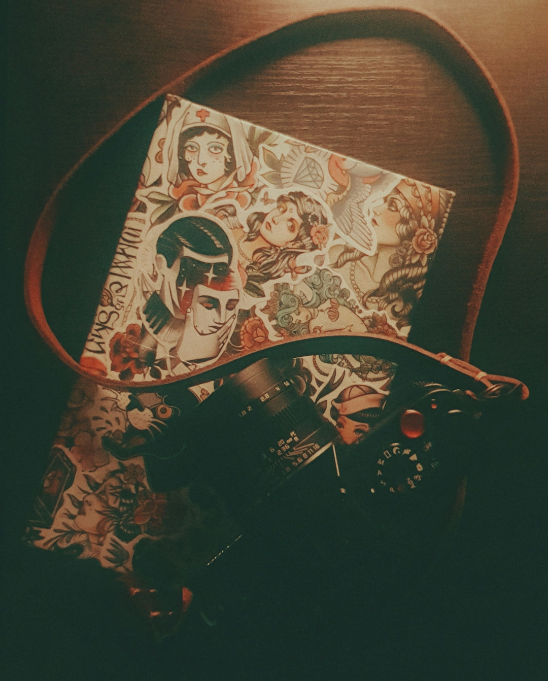Camera and tattoo-decorated notebook on a dark wooden surface