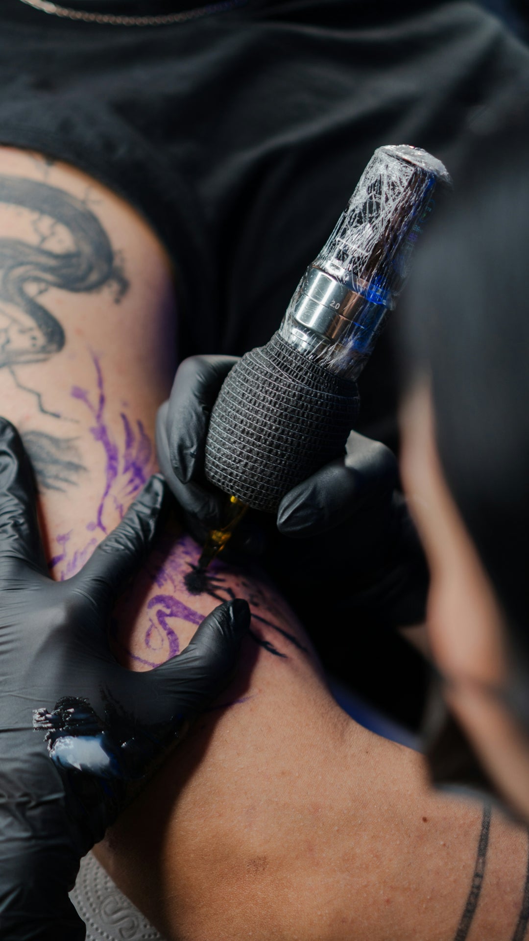 Tattoo artist applying design to skin with a machine.